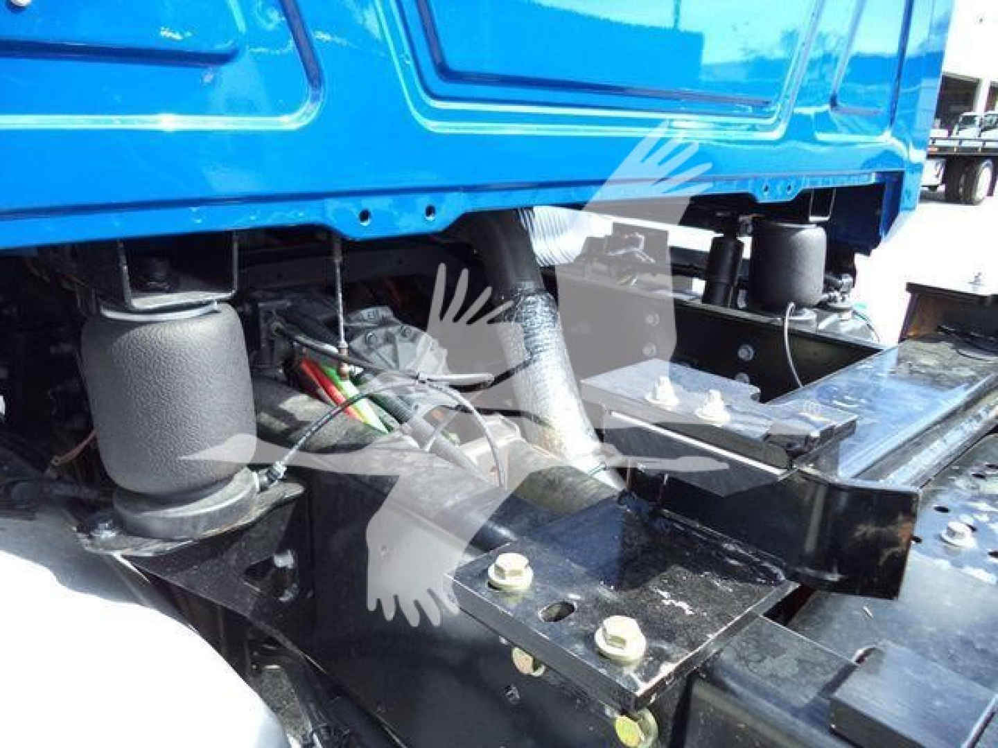 Blue Mack MD6 truck chassis with suspension components and frame rails visible, showing mounting bolts and wiring harness near the underbody