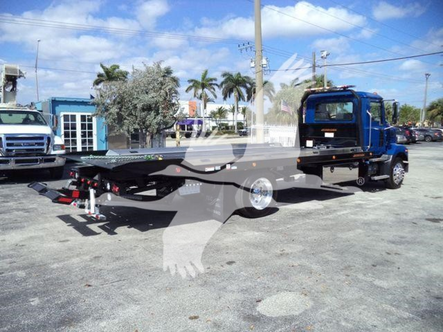 Flatbed tow truck chassis with blue cab on a lot, Mack MD6-style long flatbed and winch area visible.