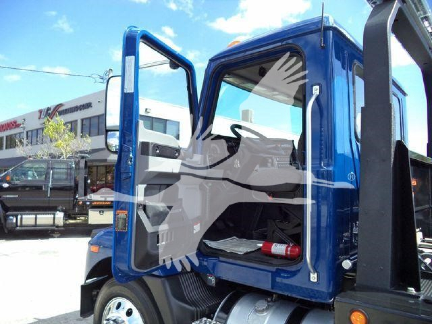 Truck cab door open showing interior of blue Mack MD6 rollback truck with white interior and black frame.
