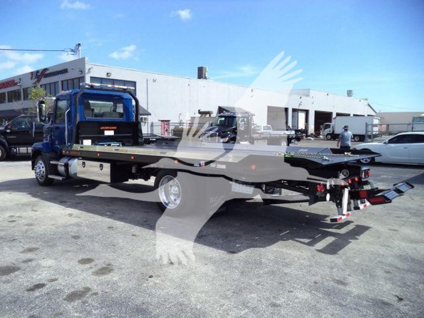 Truck bed and tow equipment on a blue Mack MD6 rollback truck, side view showing flatbed and hydraulic equipment