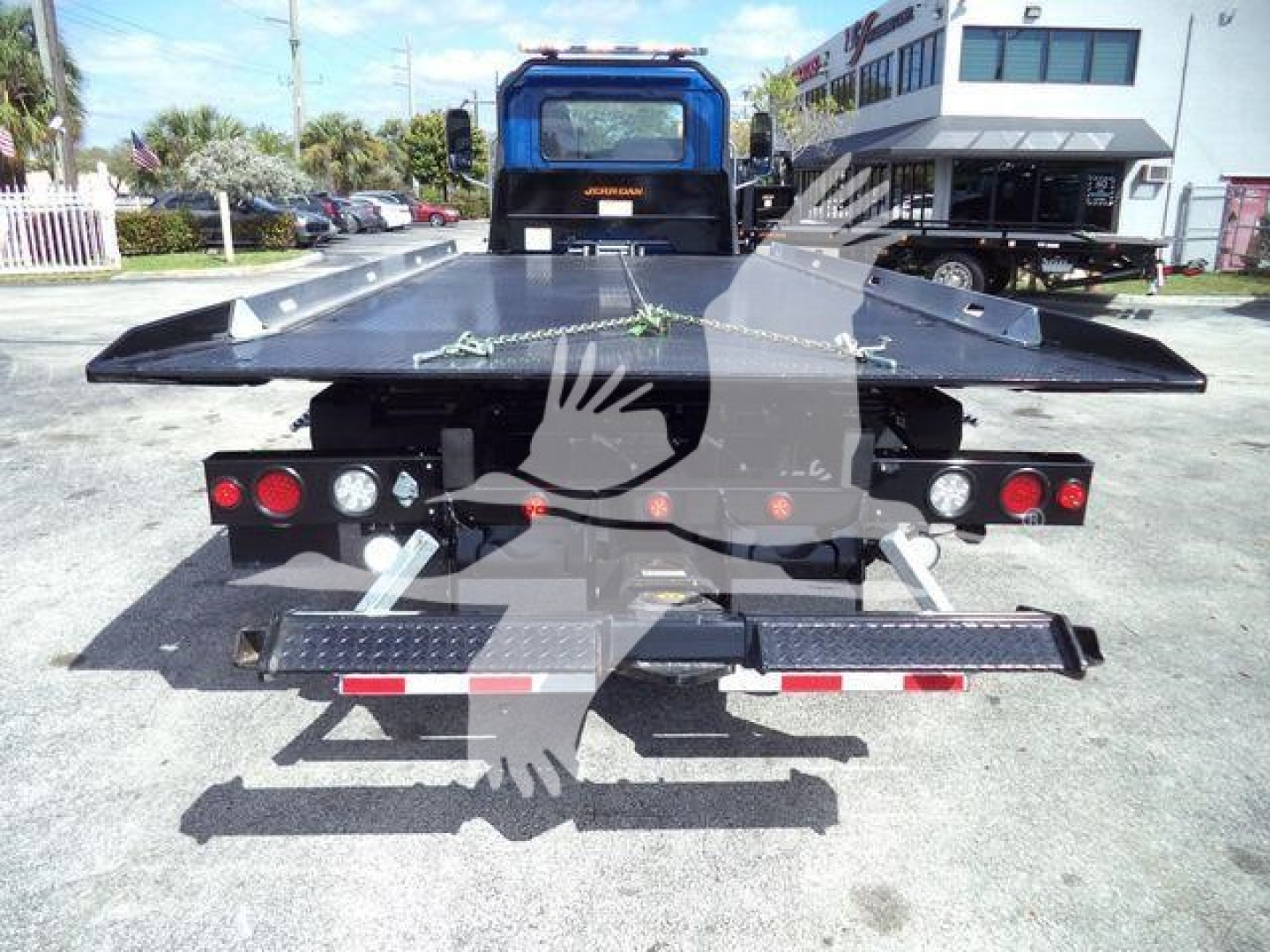 Truck rear view showing flatbed/rollback platform with taillights, safety chains, and rear bumper; Mack MD6 stock photo with equipment in dealership lot.
