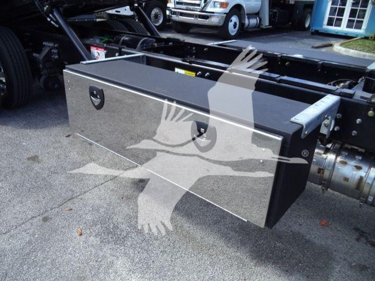 Flatbed truck undercarriage showing a large rectangular toolbox mounted on the frame.