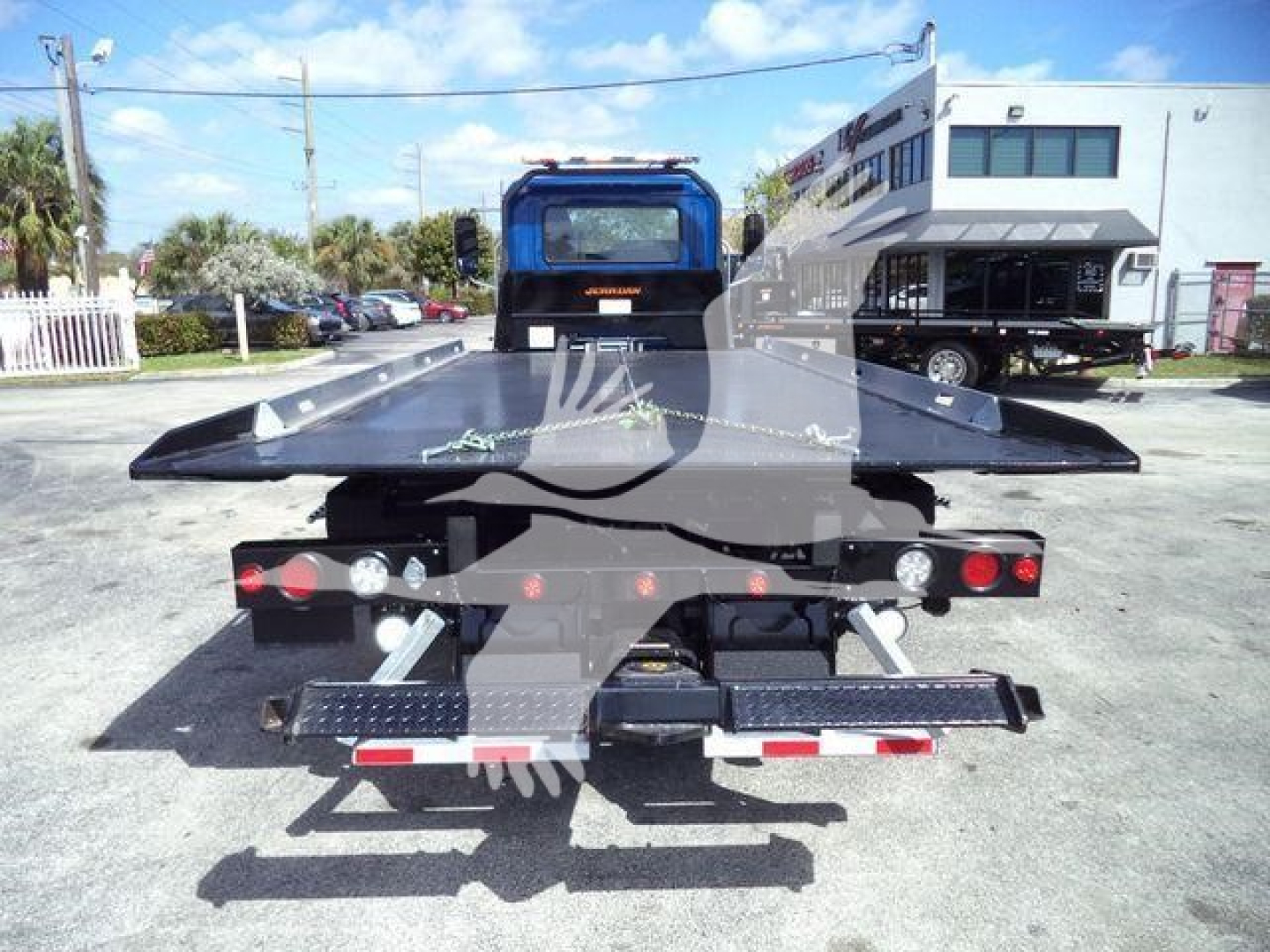 Truck bed with rollback equipment viewed from rear; flatbed steel platform, taillights, and safety rails visible.