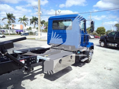 Truck cab and chassis of a 2027 Mack MD6 rollback truck showing blue cab and rear storage compartments with metal framework and hydraulic components.
