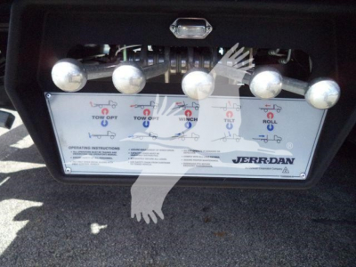 Control panel of a Jerr-Dan rollback equipment with labeled levers and illustration icons for tow/opt operations. Visible text includes 'JERR-DAN' logo and operating instruction panel.