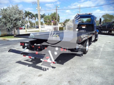 Flatbed rollback truck shown from rear/right side with loading ramps and hydraulic equipment.