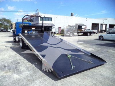 MD6 rollback tow truck with a flatbed in lowered position, blue cab, white trailer in background, open parking lot.