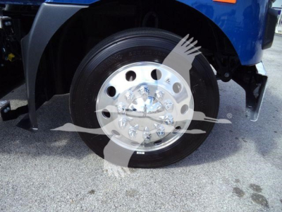 Front wheel of a blue Mack MD6 truck showing polished wheel with lug nuts and tire.