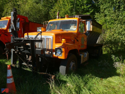 Orange 1997 International 2574 truck with sander attachment, front grille guard, and dumping bed parked in grassy area.
