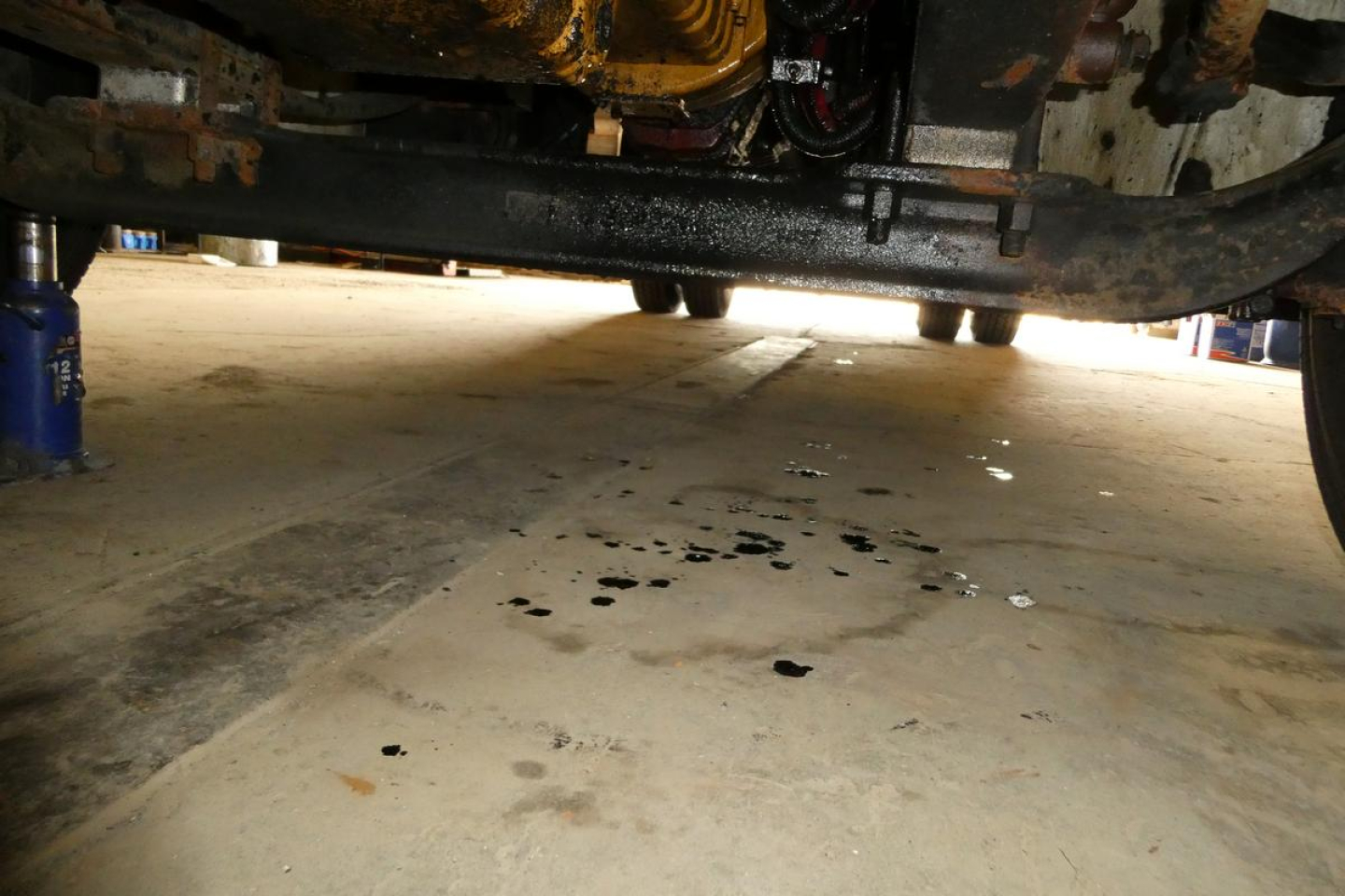 Underbody view of a Freightliner M2-106 flatbed truck showing service area and oil/fluids on concrete.