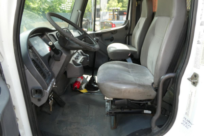 Truck cab interior of a 2006 Freightliner M2-106 showing driver seat, steering wheel, and dashboard visible with gray seats and entry door open.