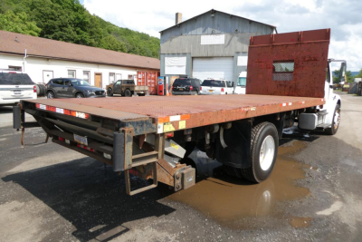 Flatbed tow truck bed with rear loading ramp and chassis, Freightliner M2-106 in a yard.