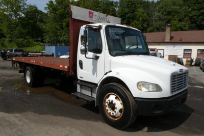 Flatbed tow truck side view showing white Freightliner M2-106 cab and long brown flatbed with black tires.
