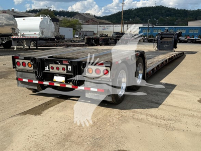 Trailer with XL Specialized logo showing a low-boy double drop expandable trailer in a yard, rear lights and metal deck visible.