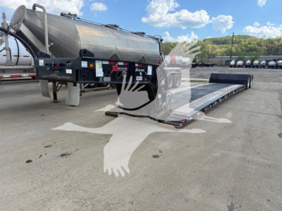 Trailer with extendable lowboy ramp in a loading yard, side view showing cylindrical tank and dual-axle trailer with hydraulic platform. Visible labels include stock number and VIN area.