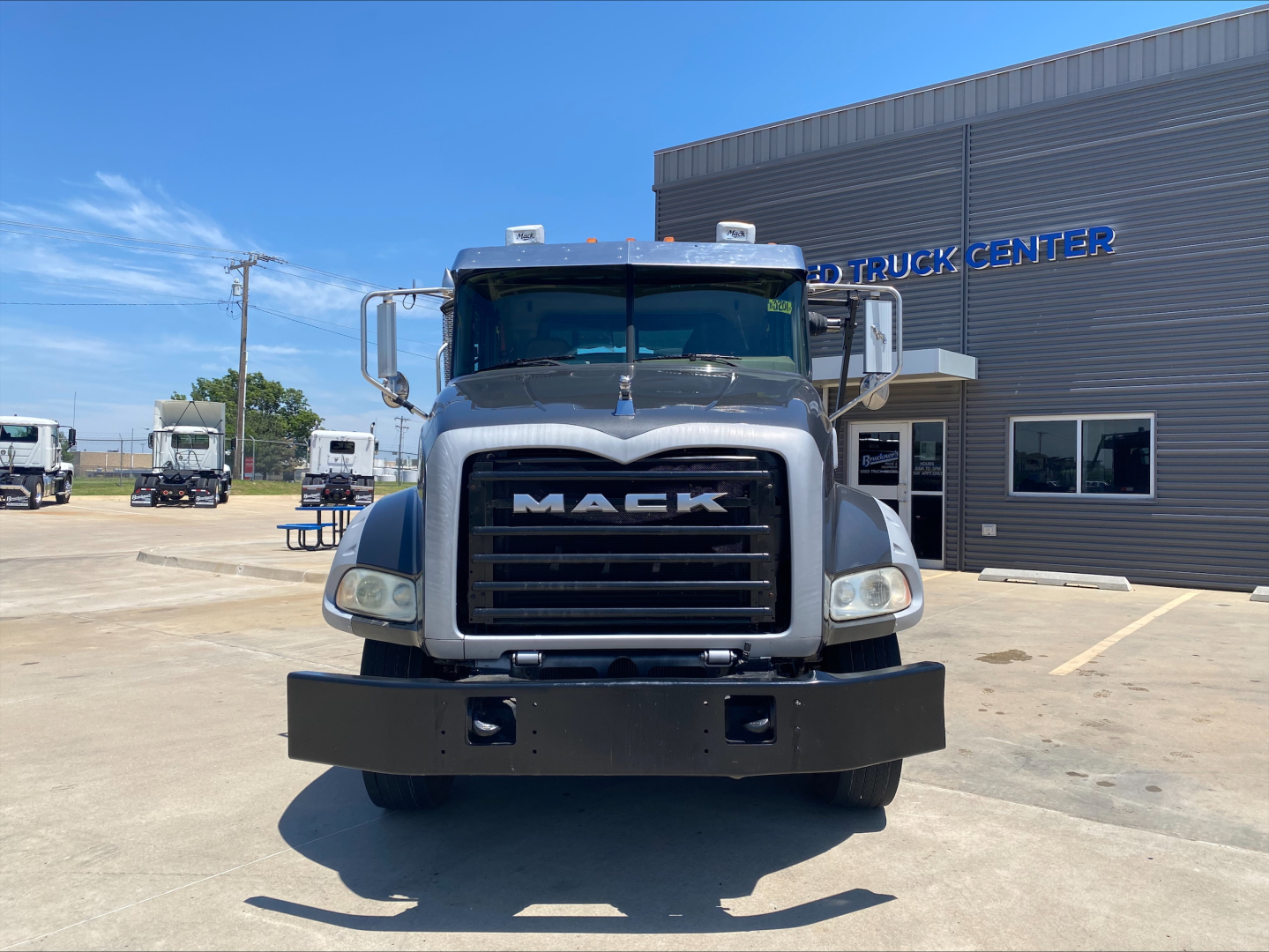 Front view of a 2016 Mack GU533 rolloff truck showing large grille with MACK lettering and bumper in a dealership lot.