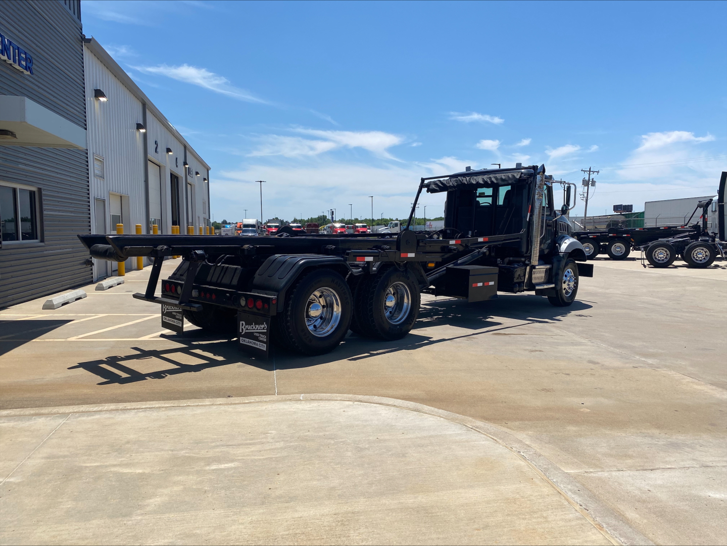2016 Mack GU533 rolloff truck side view showing flatbed with extended hitch and dual rear axles.