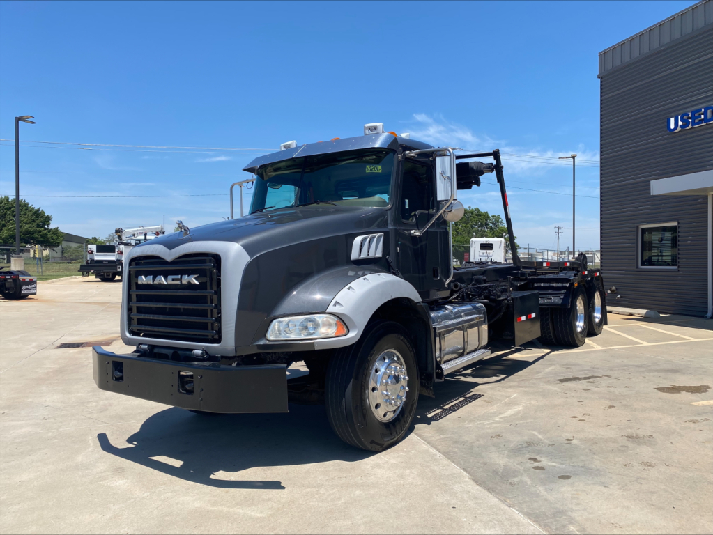 Mack GU533 dump truck in service showing front grille, cab, and chassis with flatbed roloﬀ bed; chrome wheels; Mack logo on grille.