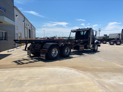 2016 Mack GU533 rolloff truck side view showing flatbed with extended hitch and dual rear axles.