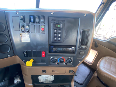 Cockpit/driver controls of a Mack GU533 truck showing gear selector with N N R D, ignition, various switches, climate controls, and a yellow caution handle.