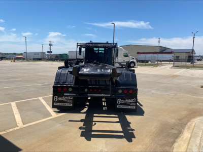 Rear view of a Mack GU533 roll-off truck showing rear bumper, taillights, and license plate frames with text. Visible: Bruckners Oklahoma City plates on both sides, rear window, and shadow of the truck on pavement.