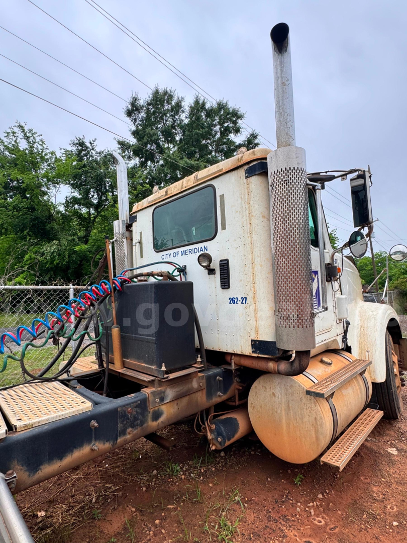 Truck sleeper cab and rear view showing vertical exhaust stacks and fuel tanks in a roll-off truck configuration.