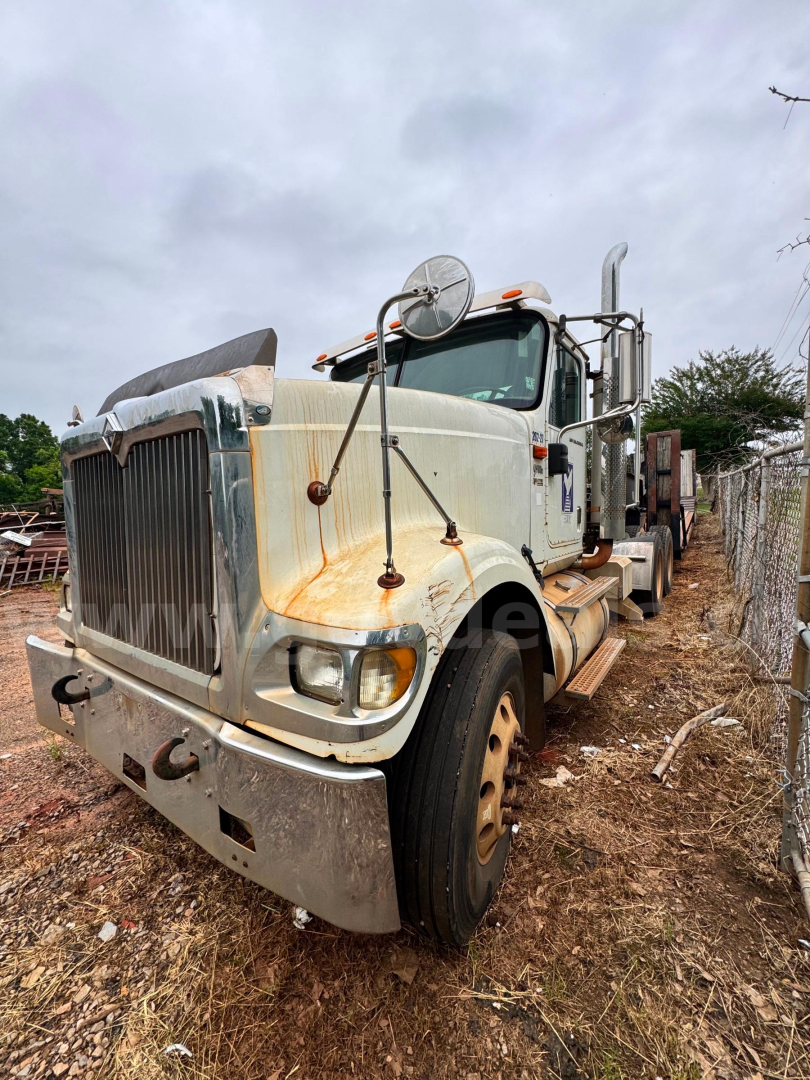 Heavy-duty truck cab view of a white 2007 International 9900i with rust accents, large grille, side mirrors, and sleeper cab; front wheels on dirt at yard.