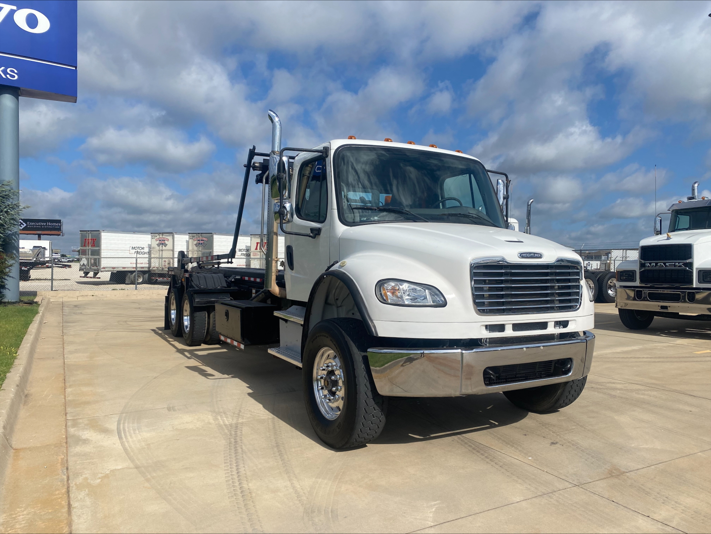 2019 Freightliner M2 roll-off truck on lot showing cab and flatbed, front grille, headlights, large chrome bumper, and dual rear axles.