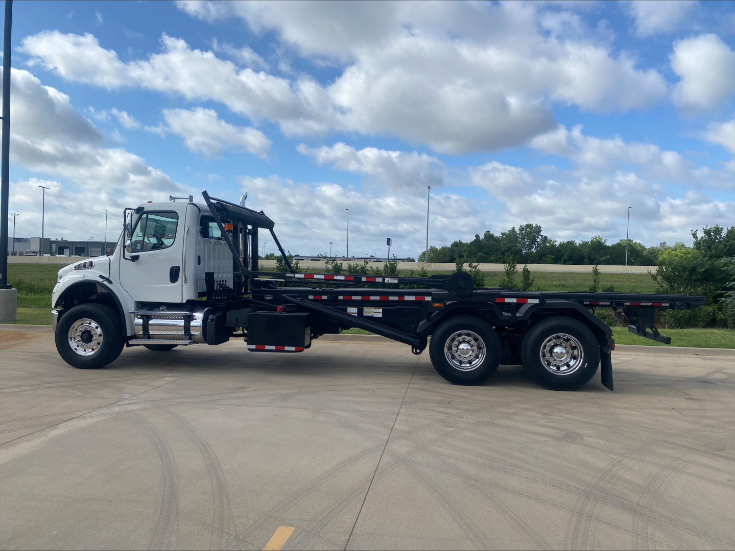 2019 Freightliner M2 roll-off truck side view showing long black flatbed and white cab with crane apparatus