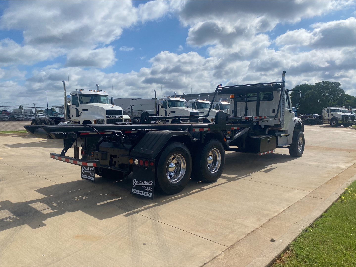 2019 Freightliner M2 roll-off truck with flatbed and empty chassis, side view showing dual rear axles and wheel mudflaps.
