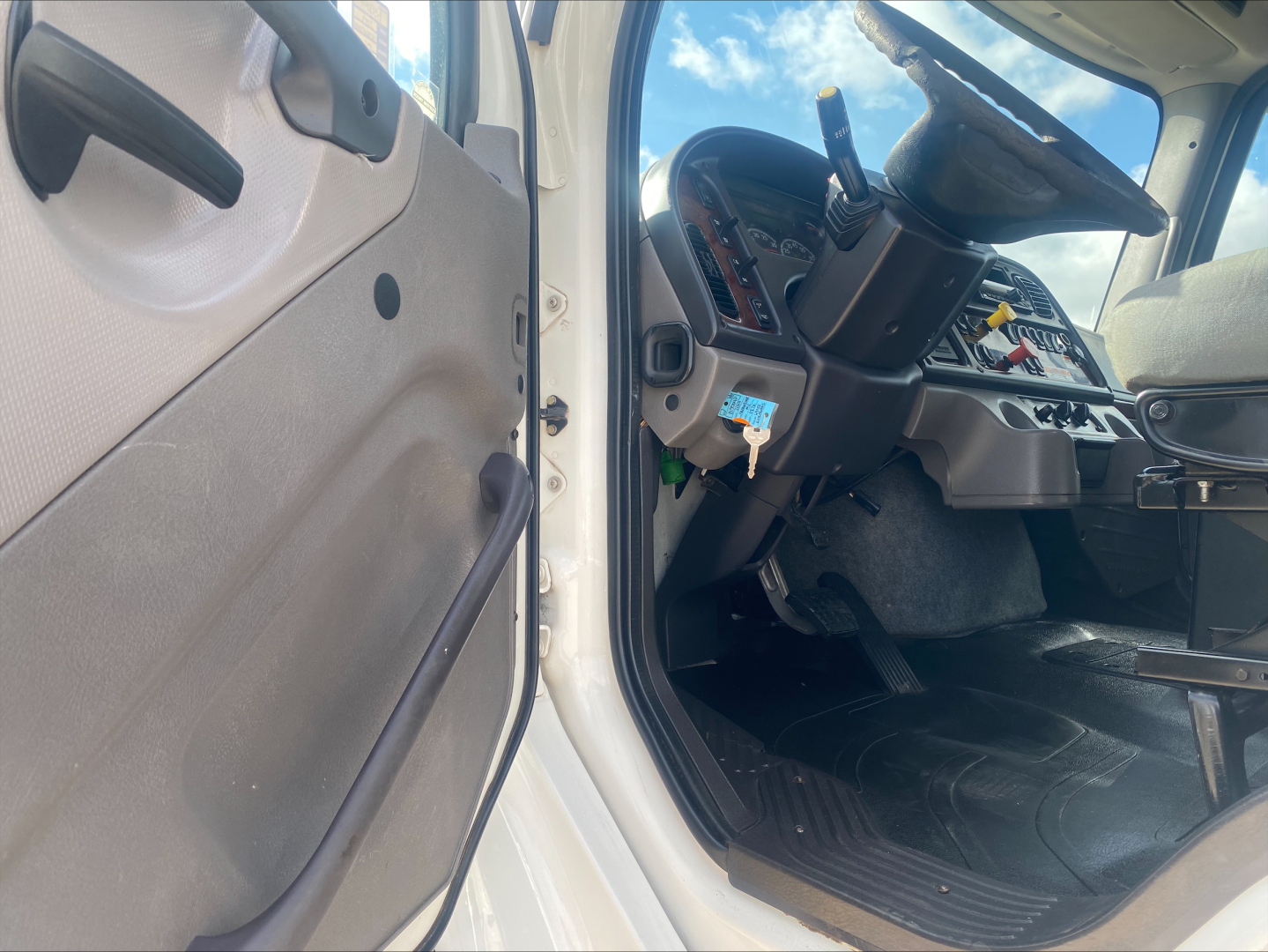 Cab interior of a 2019 Freightliner M2 rolloff truck showing steering wheel, dashboard, pedals, and driver's door area.