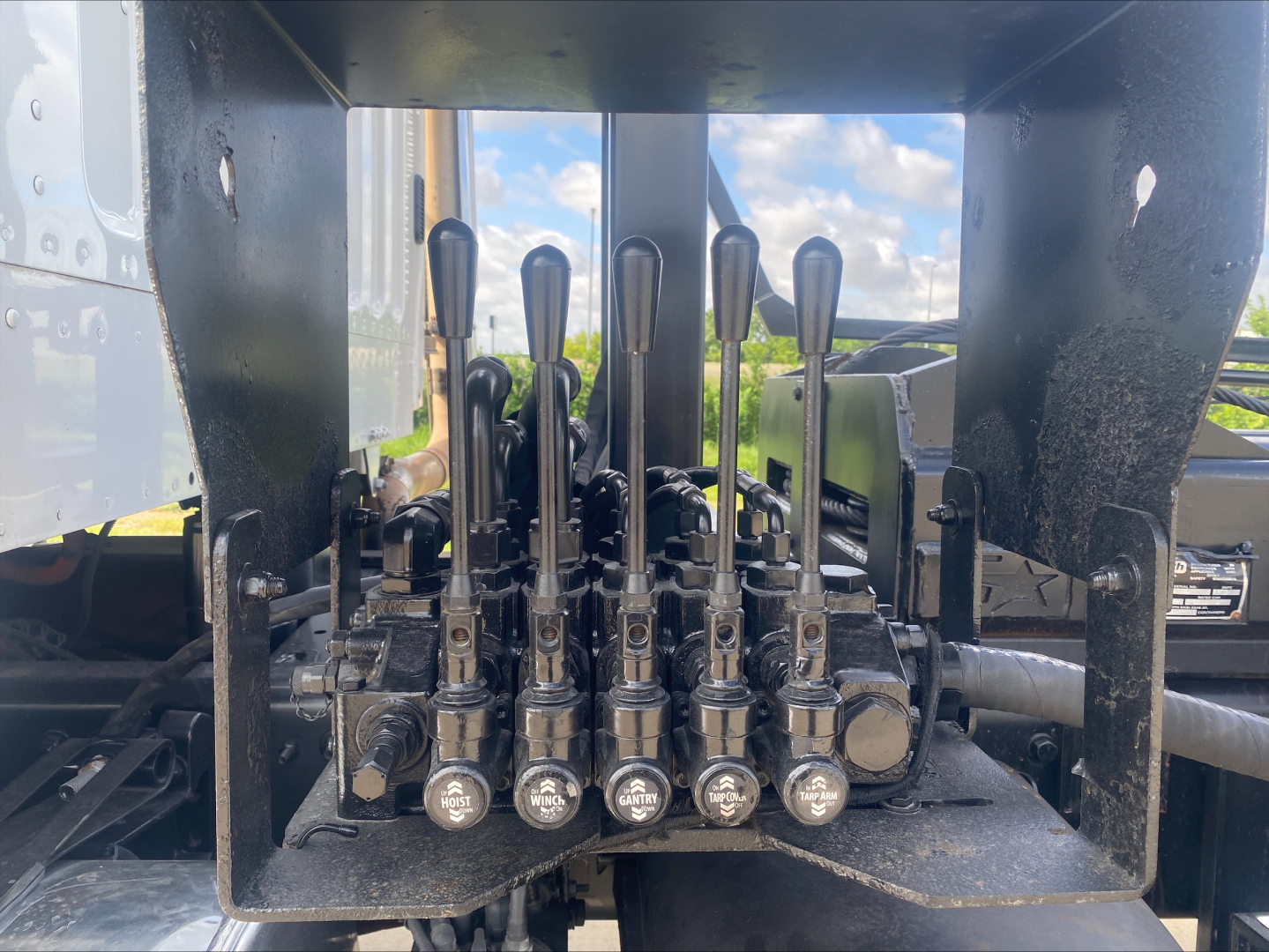 View of Freightliner M2 operator levers arranged in a row under a control panel with multiple hydraulic levers and caps labeled L, R, and other control icons.
