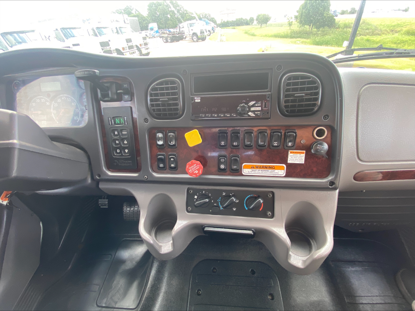 Dashboard of 2019 Freightliner M2 cab interior showing steering wheel, instrument cluster, center console with switches, climate controls, and radio cavity.