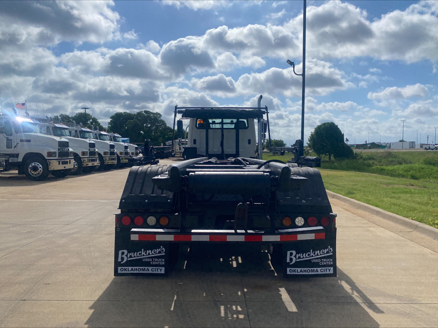 Freightliner M2 roll-off truck rear view showing bumper, taillights, hydraulic system, and rear mud flaps with Bruckner’s Oklahoma City branding.