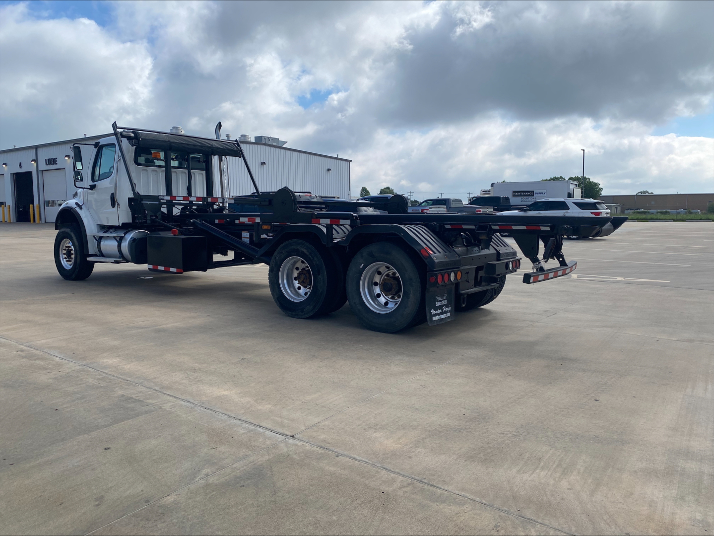 2019 Freightliner M2 roll-off truck side view showing dual rear axles, flatbed frame, and equipment cradle.