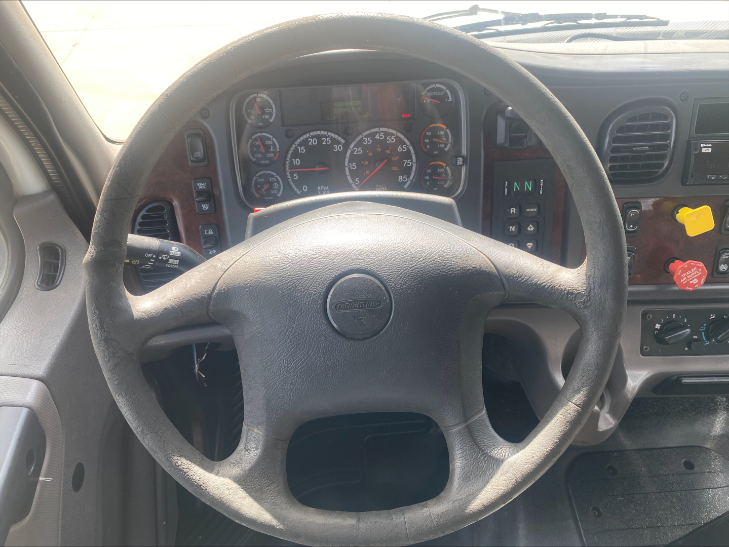 Volvo/Freightliner M2 steering wheel and instrument cluster in cab showing gauges and dashboard controls.