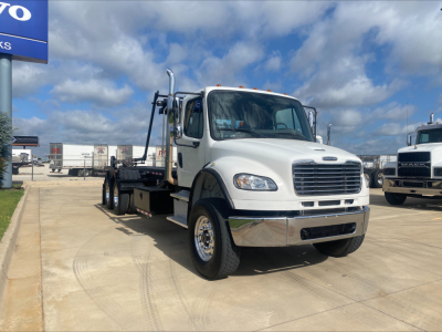 2019 Freightliner M2 roll-off truck on lot showing cab and flatbed, front grille, headlights, large chrome bumper, and dual rear axles.