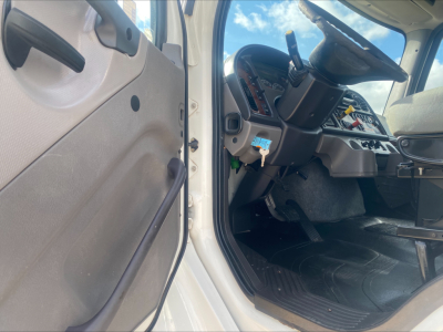 Cab interior of a 2019 Freightliner M2 rolloff truck showing steering wheel, dashboard, pedals, and driver's door area.
