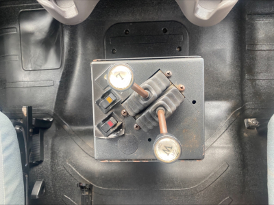 Truck interior showing hydraulic valve control panel with two gauges and copper tubes on a Freightliner M2 rolloff system.