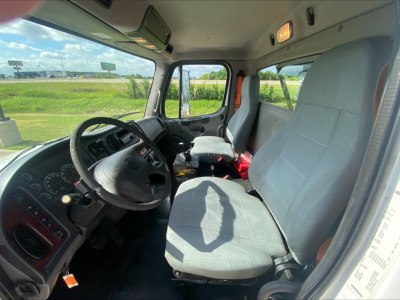 Cab interior of a 2019 Freightliner M2 roll-off truck showing steering wheel, dashboard, driver seat, and passenger seat.