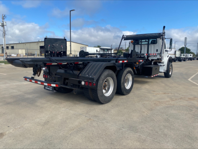 Freightliner M2 roll-off truck chassis showing rear and side, with dual rear axles, black chassis, and white cab.