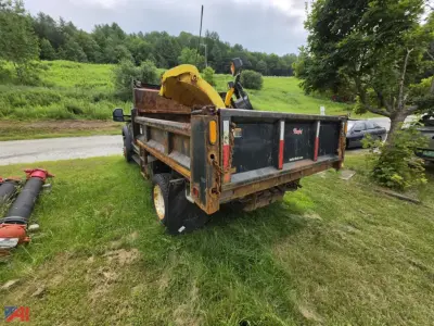 Dump truck bed of a 2017 Ford F-550 Super Duty dump truck with a rusted metal bed and yellow hydraulic components, parked on grass with trees and a road in the background.