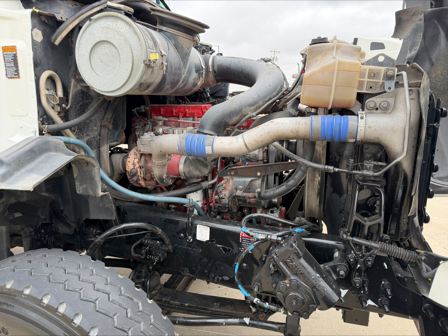 MacK GU533 engine bay showing large turbo and hoses, radiator, coolant reservoir, and wiring harness in front-left side.