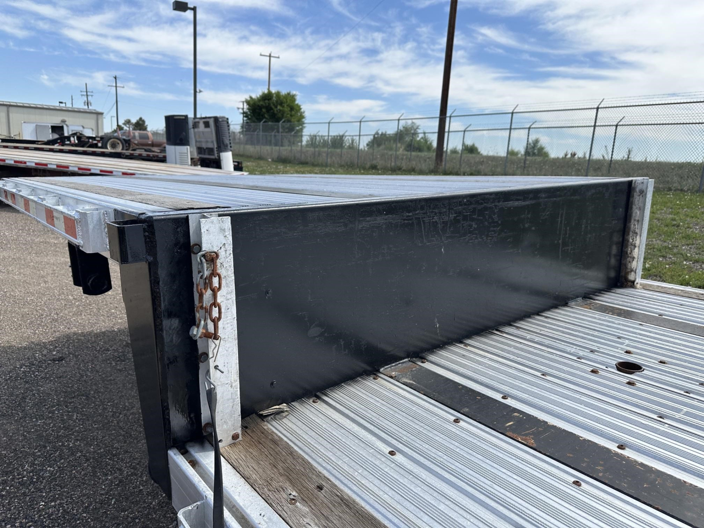 Combo spread air drop deck trailer side view showing gray steel deck plates and black cross beam with chain and holes along edge.