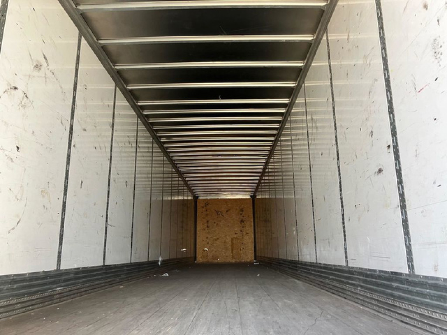 Trailer interior showing empty cargo area with metal side ribs and overhead ribs, white walls, wooden back wall, and wooden floor in a Stoughton van.