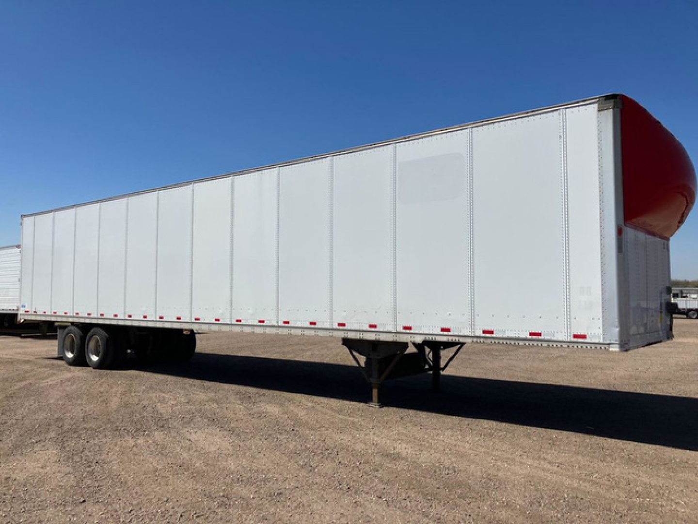 Van trailer in profile showing a long white curtain-side trailer with dual rear axles and a red rounded nose cap on the front. No visible text on the trailer surface.