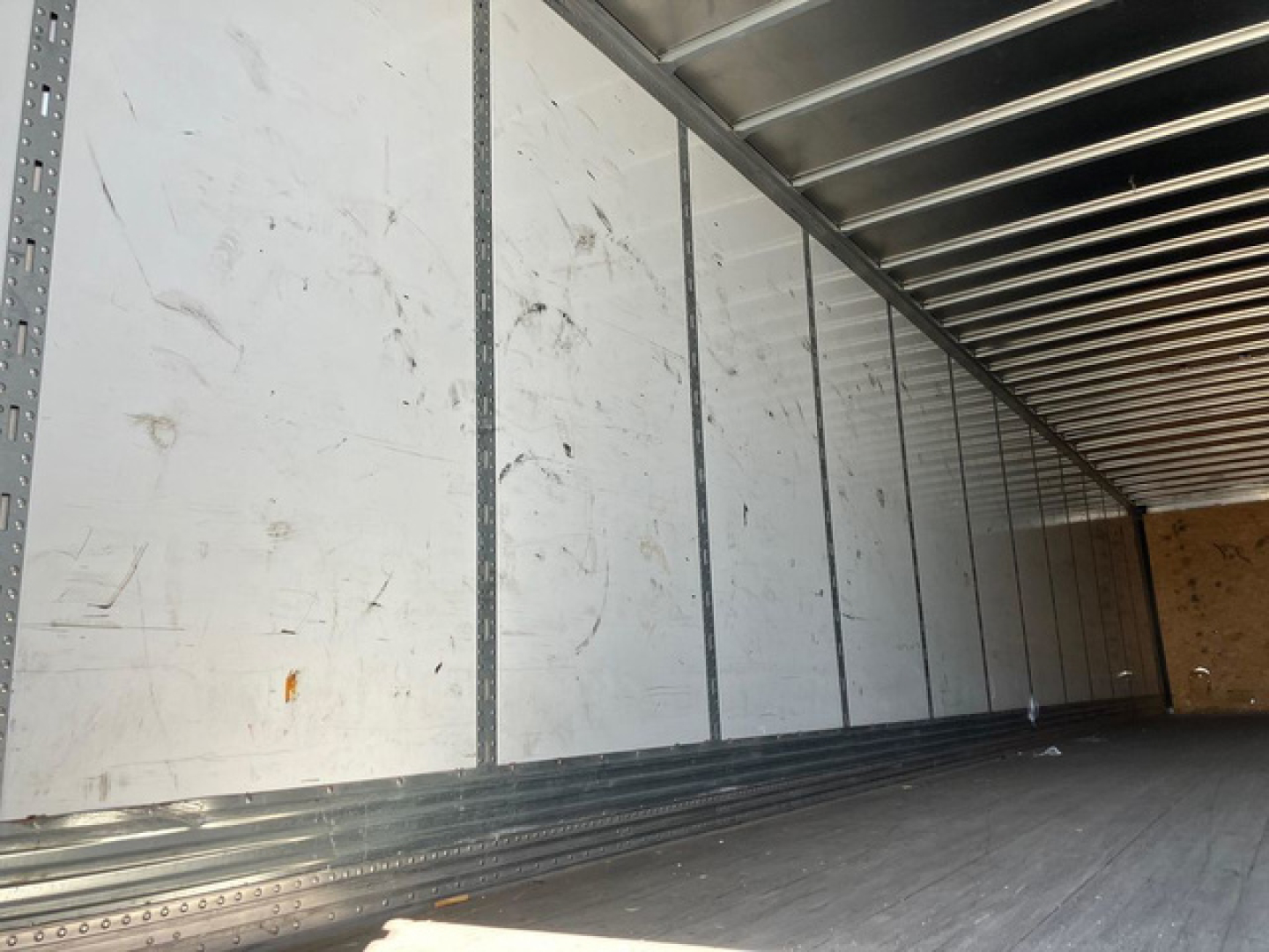 Van trailer interior showing metal sidewalls and ribbed ceiling, empty cargo area with wooden rear wall, interior marks and scratches.
