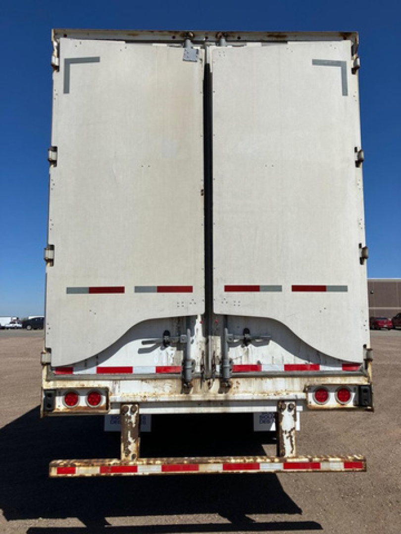 Rear view of a white Stoughton van trailer showing double doors with hinges, latches, and red reflective strips; dirt and minor wear visible on lower bumper area.