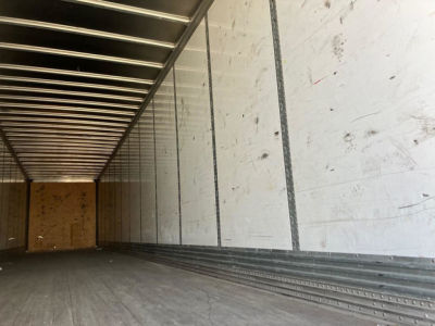 Trailer interior showing empty cargo space with ribbed aluminum walls and floor, rear wooden bulkhead, side rails.