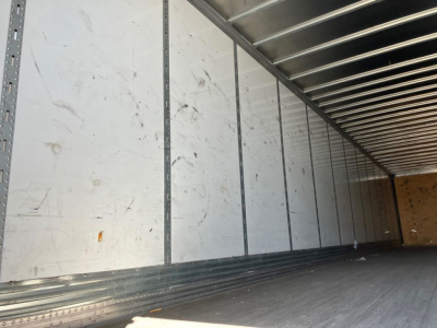 Van trailer interior showing metal sidewalls and ribbed ceiling, empty cargo area with wooden rear wall, interior marks and scratches.